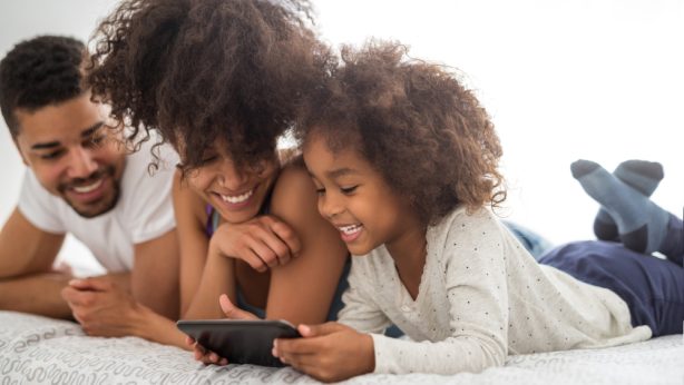 Happy young family laying on a bed with a tablet